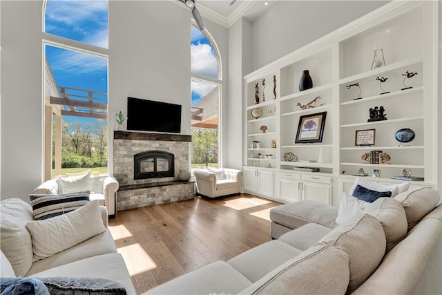 living area featuring a glass covered fireplace, wood finished floors, a towering ceiling, and ornamental molding