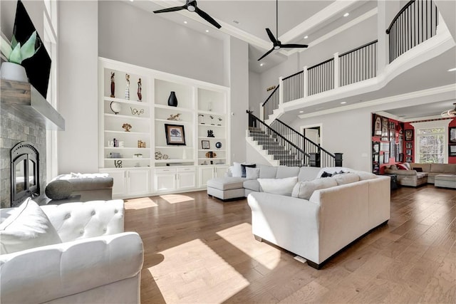 living room featuring a ceiling fan, hardwood / wood-style flooring, a towering ceiling, a fireplace, and recessed lighting