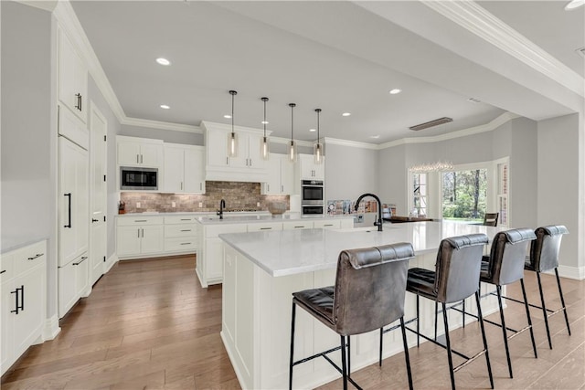 kitchen featuring a large island with sink, stainless steel appliances, backsplash, light countertops, and light wood-type flooring