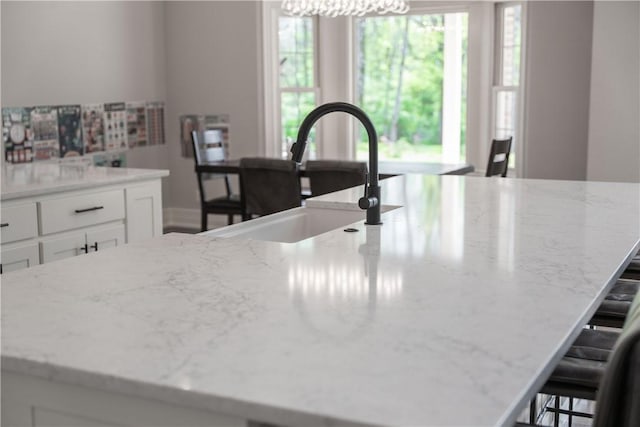 kitchen featuring white cabinets, a kitchen bar, light stone counters, and a sink