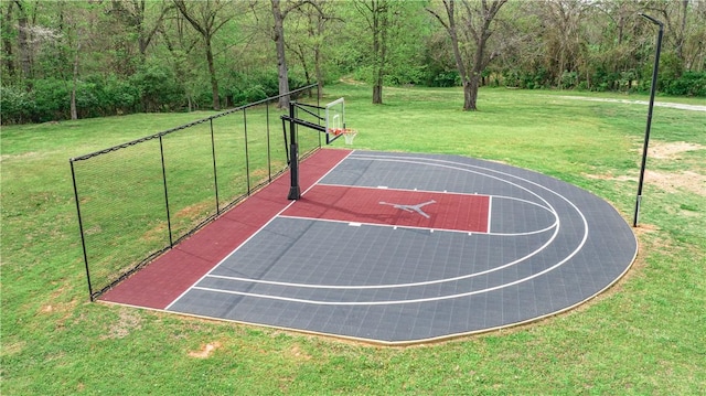 view of basketball court featuring basketball court, a view of trees, a lawn, and fence