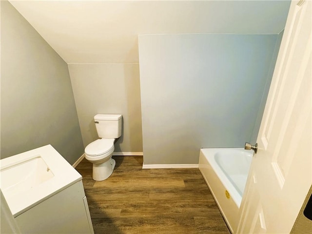 full bath featuring wood finished floors, a bath, vanity, baseboards, and toilet