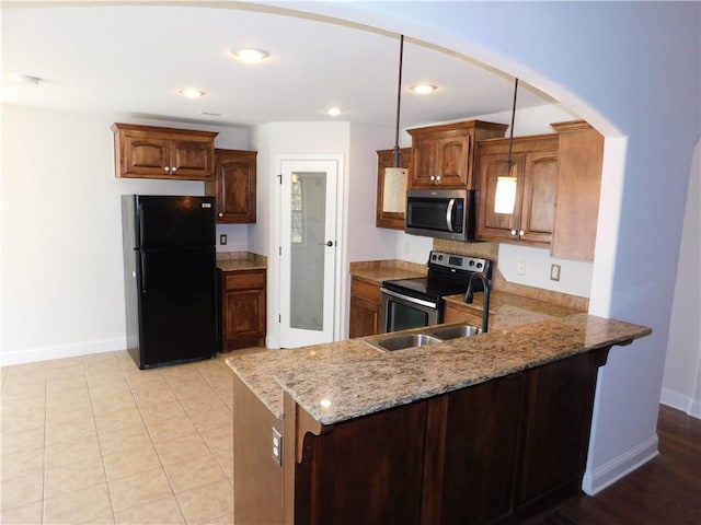 kitchen featuring light stone counters, a sink, stainless steel appliances, baseboards, and a peninsula