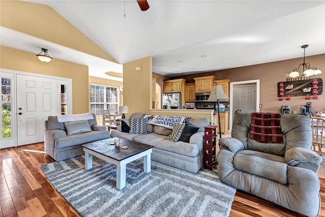 living area with vaulted ceiling, ceiling fan with notable chandelier, and light wood-style flooring