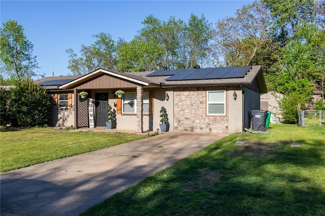 ranch-style home with roof mounted solar panels, stone siding, driveway, and a front yard