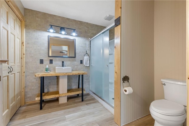 bathroom featuring toilet, wood finished floors, a shower stall, vanity, and rail lighting