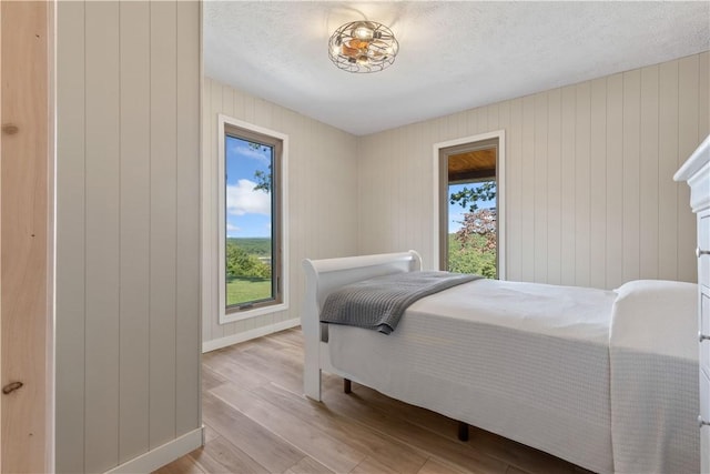 bedroom featuring wooden walls, baseboards, a textured ceiling, and light wood-style floors