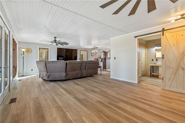 living room featuring a barn door, baseboards, a ceiling fan, and light wood finished floors