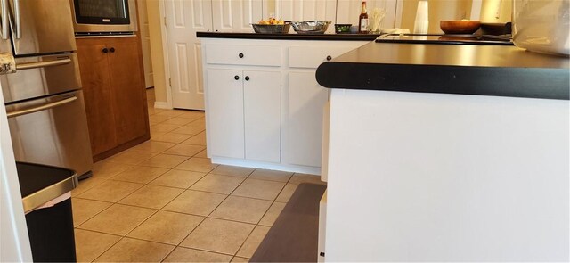 kitchen featuring freestanding refrigerator, wall oven, white cabinetry, and light tile patterned floors