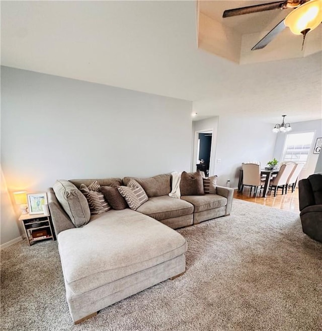 carpeted living area with baseboards and ceiling fan with notable chandelier