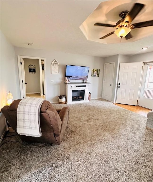 carpeted living room featuring baseboards, a fireplace, and ceiling fan