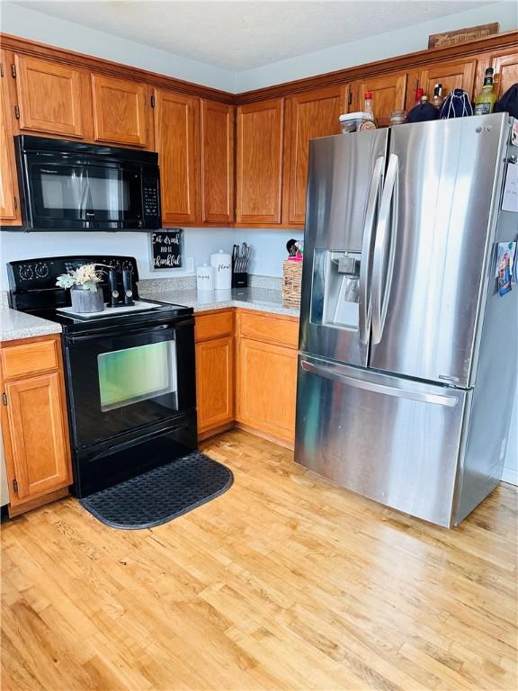 kitchen with light wood-type flooring, brown cabinetry, light countertops, and black appliances