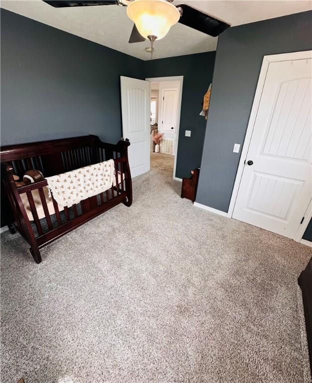 bedroom with carpet flooring, baseboards, a ceiling fan, and a crib