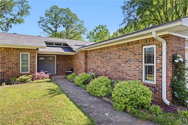 property entrance with a lawn, brick siding, and roof with shingles
