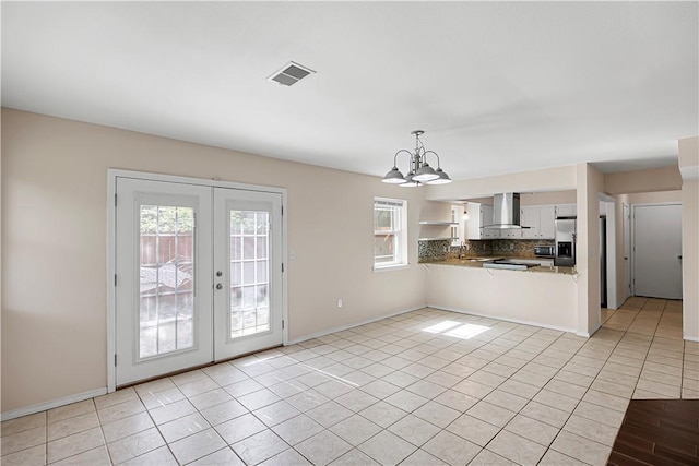 kitchen with wall chimney range hood, tasteful backsplash, a chandelier, french doors, and a peninsula