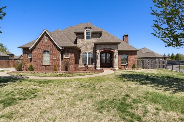 french country style house featuring fence, a chimney, brick siding, and a front yard