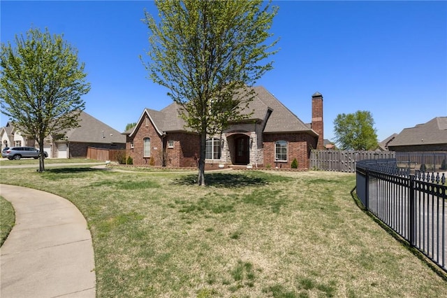 tudor-style house with a chimney, fence, a front yard, and brick siding