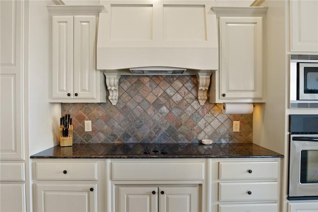 kitchen featuring dark stone counters, white cabinets, premium range hood, backsplash, and appliances with stainless steel finishes