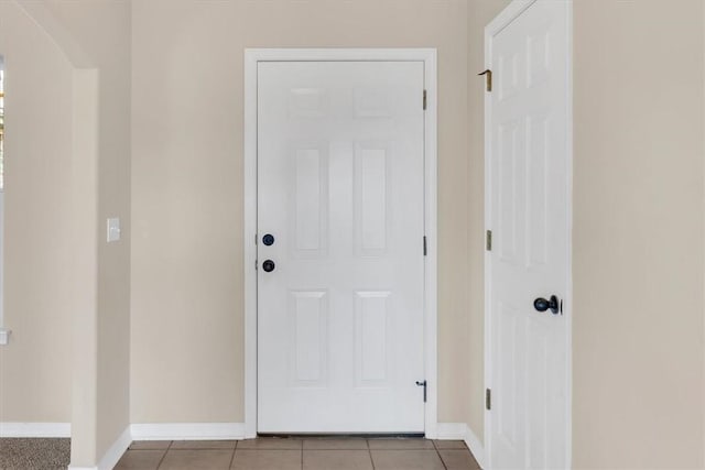 doorway with arched walkways, baseboards, and light tile patterned floors