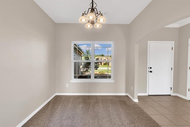 carpeted empty room featuring baseboards, tile patterned flooring, and an inviting chandelier