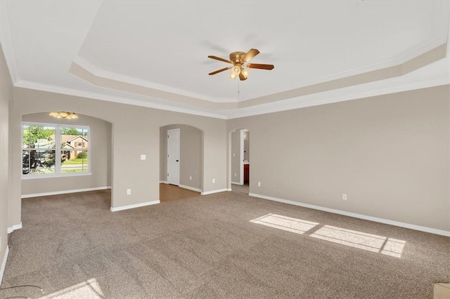 unfurnished room with a tray ceiling, arched walkways, carpet flooring, and a ceiling fan