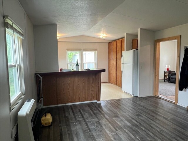 kitchen featuring wood finished floors, brown cabinets, a peninsula, lofted ceiling, and freestanding refrigerator