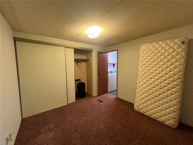 unfurnished bedroom featuring carpet flooring, a textured ceiling, a closet, and washer / dryer