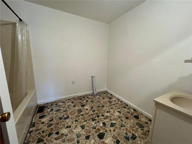 interior space featuring shower / bath combination with curtain, baseboards, vanity, and stone floors