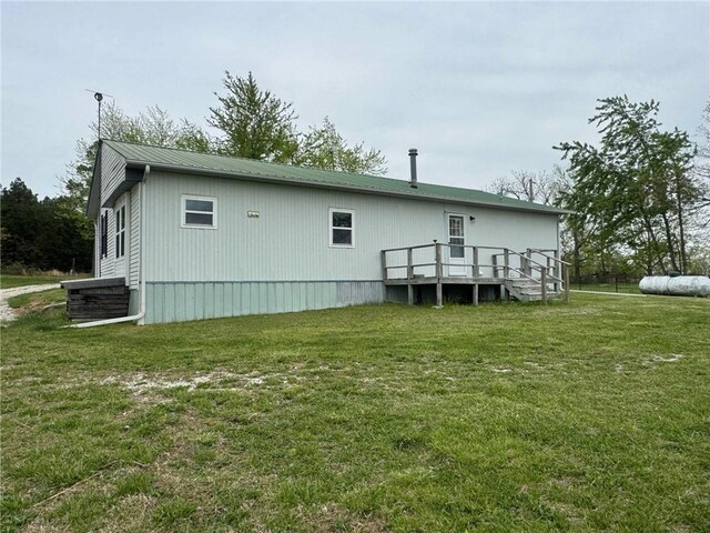 rear view of house featuring a lawn, central AC unit, metal roof, and a deck