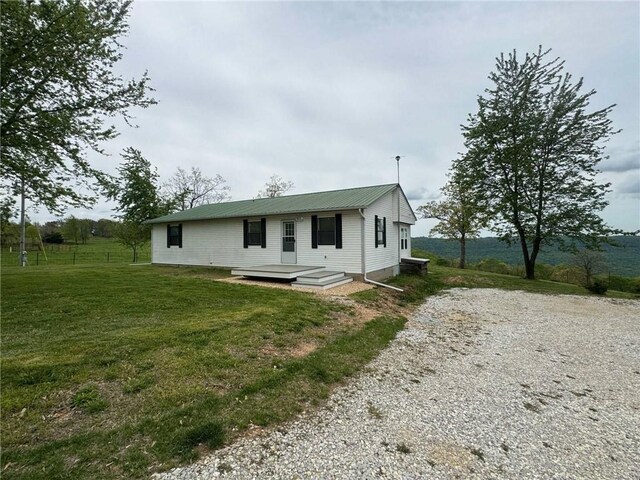 back of property featuring a lawn, gravel driveway, fence, and metal roof