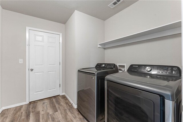washroom featuring wood finished floors, laundry area, baseboards, visible vents, and independent washer and dryer