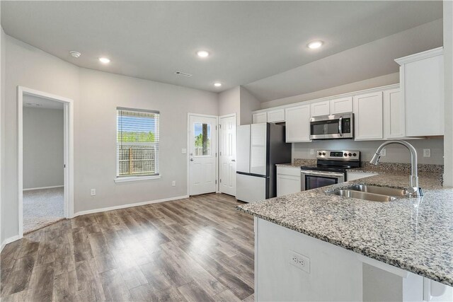kitchen featuring white cabinets, wood finished floors, a sink, light stone countertops, and appliances with stainless steel finishes