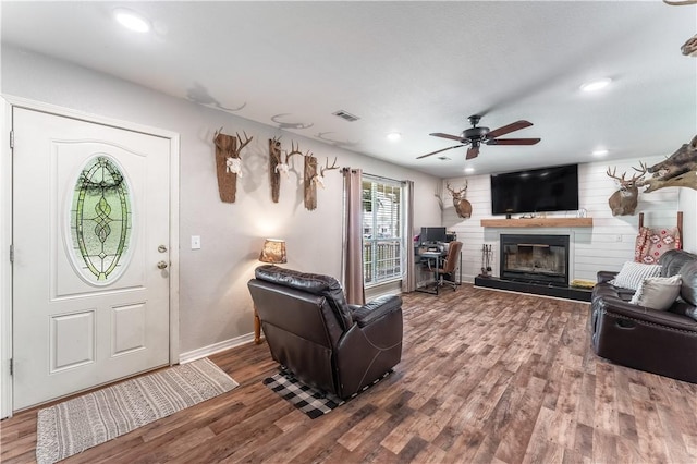 living area featuring wood finished floors, visible vents, a ceiling fan, baseboards, and a fireplace