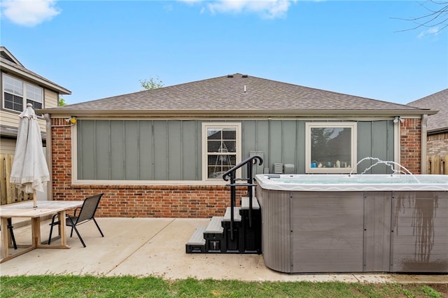 back of property featuring roof with shingles, board and batten siding, a patio, brick siding, and a hot tub