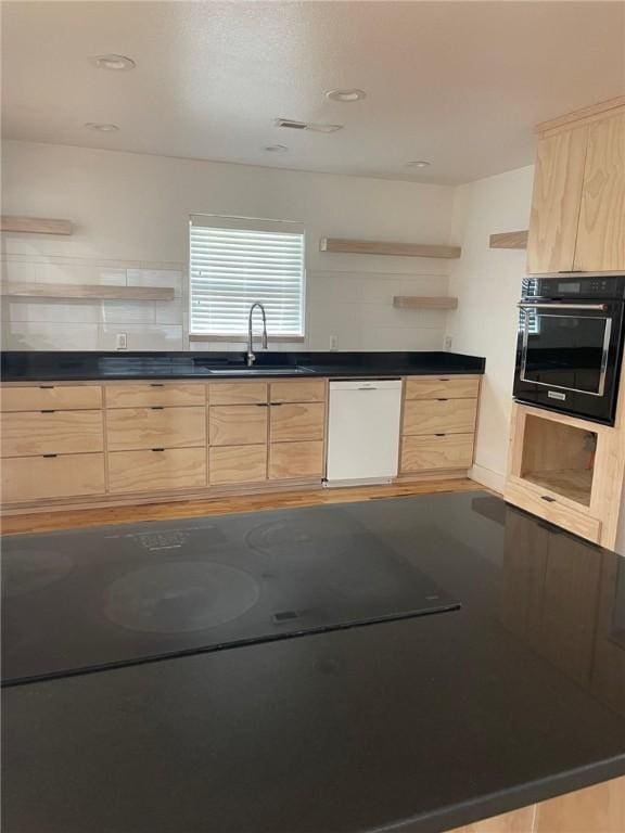 kitchen featuring oven, dark countertops, dishwasher, light brown cabinets, and a sink