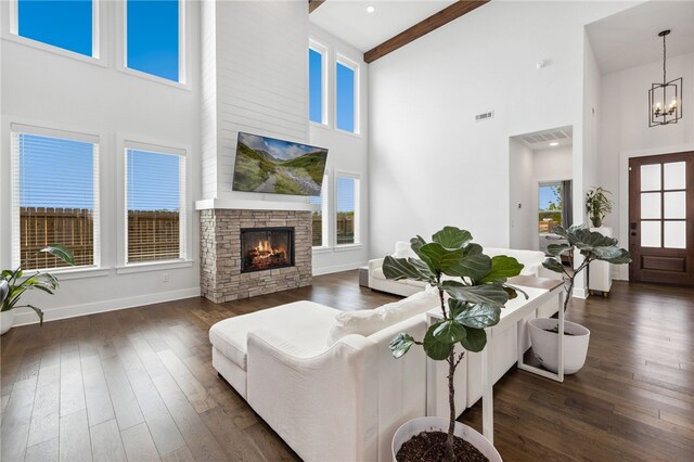 living area with visible vents, an inviting chandelier, dark wood-type flooring, a stone fireplace, and a high ceiling