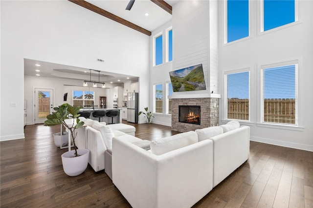living room featuring beamed ceiling, ceiling fan, dark wood-style flooring, baseboards, and a towering ceiling