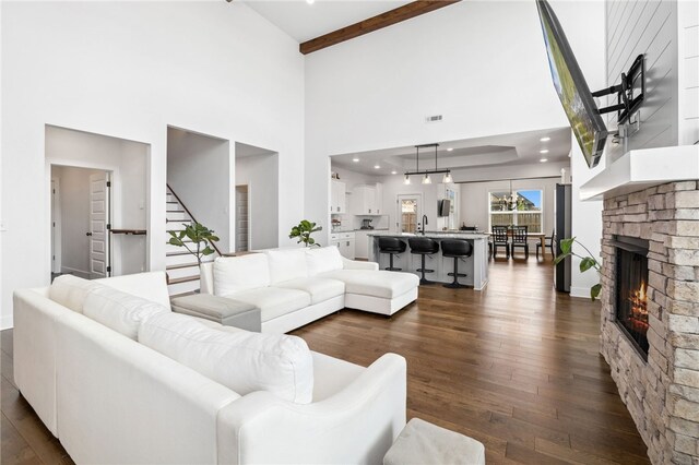 living area with a fireplace, a towering ceiling, stairway, and dark wood finished floors