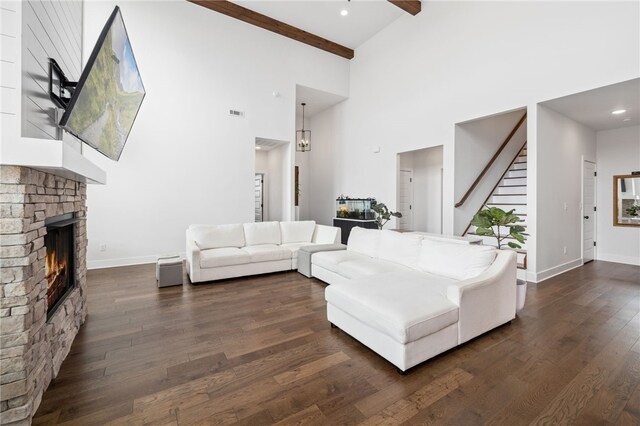 living room featuring dark wood finished floors, a lit fireplace, beam ceiling, stairway, and a high ceiling