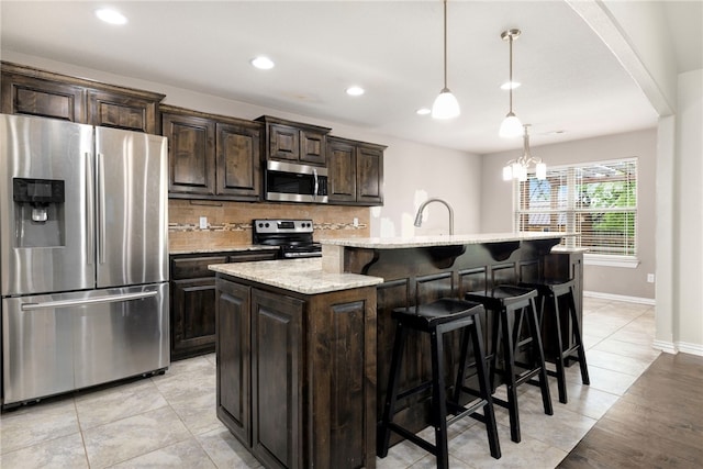 809 Sedgwick Dr, Prairie Grove, AR 72753 - kitchen with a kitchen island with sink, stainless steel appliances, a kitchen breakfast bar, backsplash, and dark brown cabinets