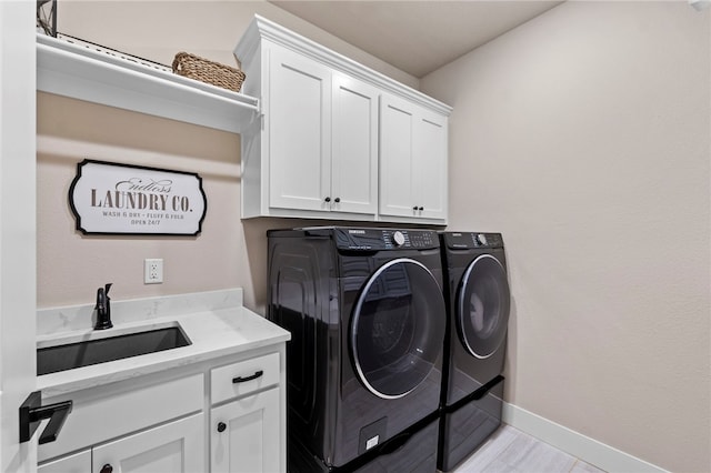clothes washing area featuring a sink, cabinet space, washing machine and clothes dryer, and baseboards