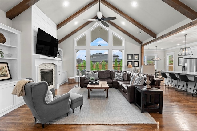 living room featuring beamed ceiling, a stone fireplace, ceiling fan, and dark wood finished floors