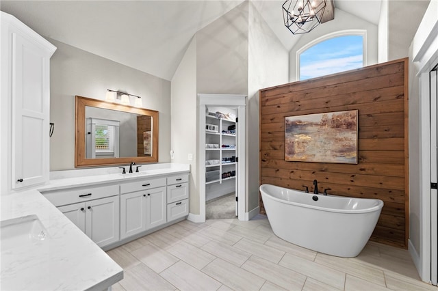 full bathroom featuring a soaking tub, vaulted ceiling, vanity, a notable chandelier, and a walk in closet