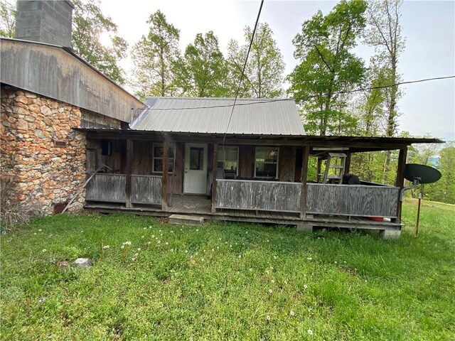 rear view of house featuring a lawn, covered porch, metal roof, and stone siding
