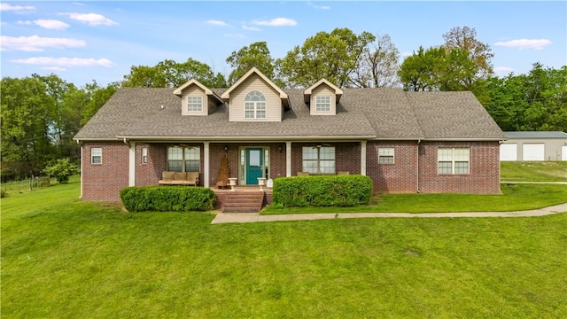 new england style home featuring a detached garage, brick siding, a shingled roof, and a front lawn