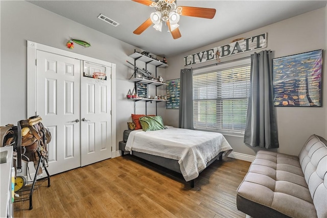 bedroom with baseboards, visible vents, wood finished floors, and a closet