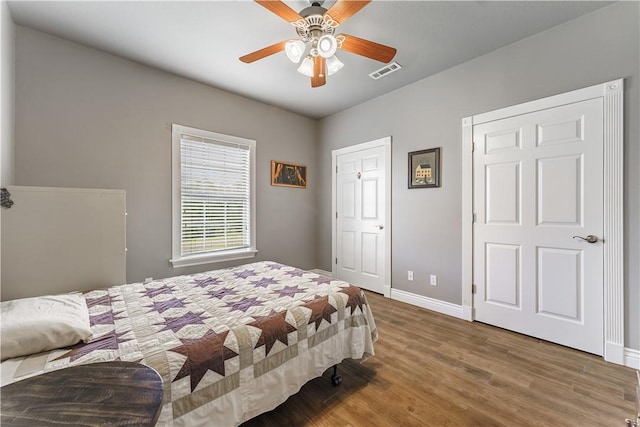 bedroom with wood finished floors, visible vents, a ceiling fan, and baseboards