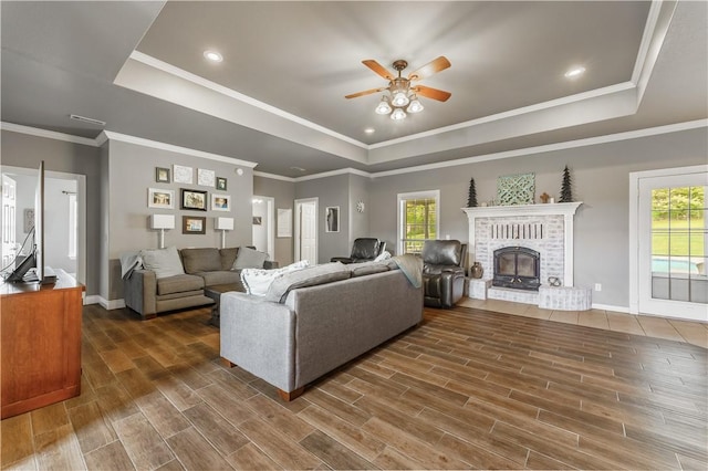 living area with a healthy amount of sunlight, a raised ceiling, a ceiling fan, and wood finished floors