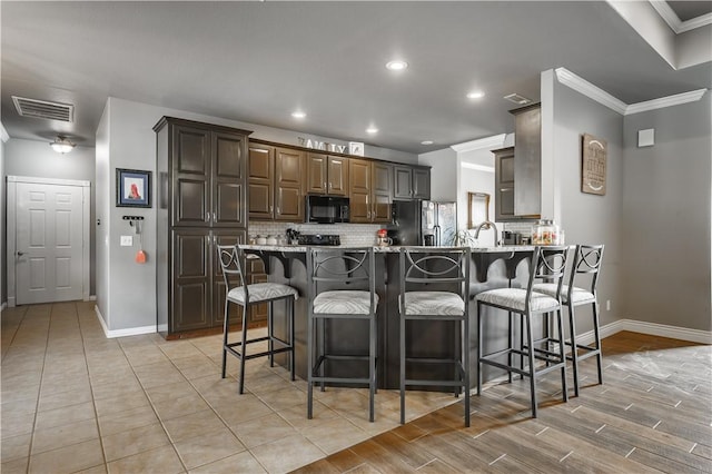 kitchen with decorative backsplash, black appliances, visible vents, a peninsula, and baseboards