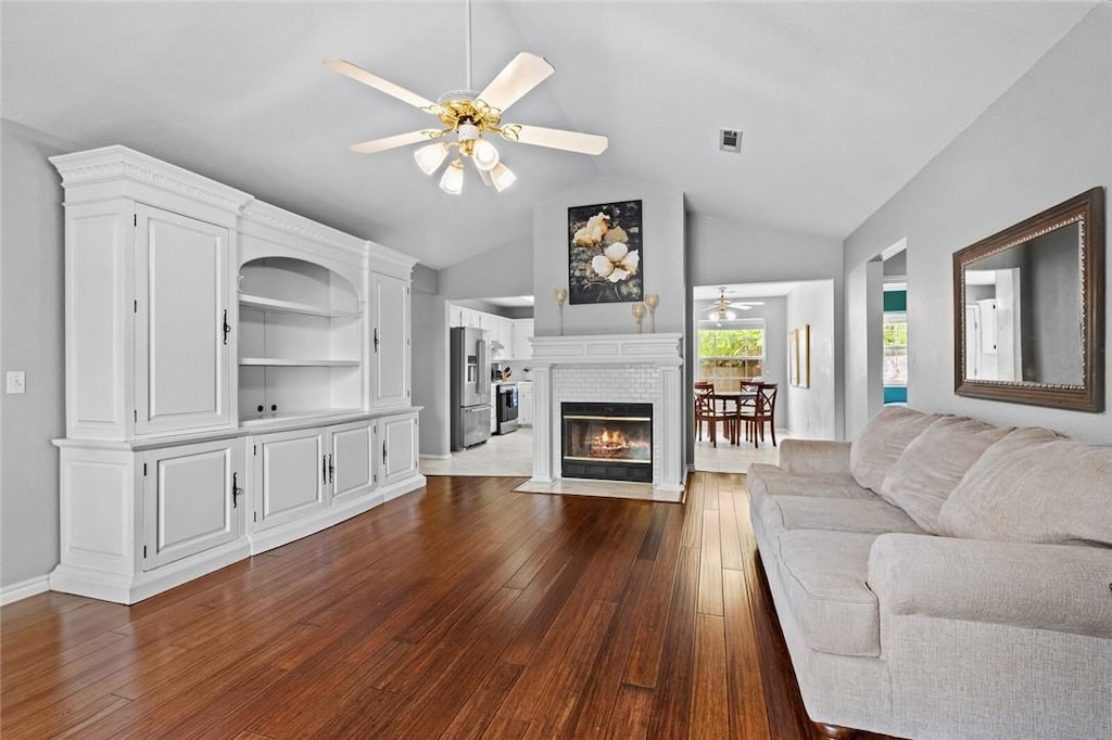 living room with a fireplace with flush hearth, a ceiling fan, dark wood-style flooring, and vaulted ceiling
